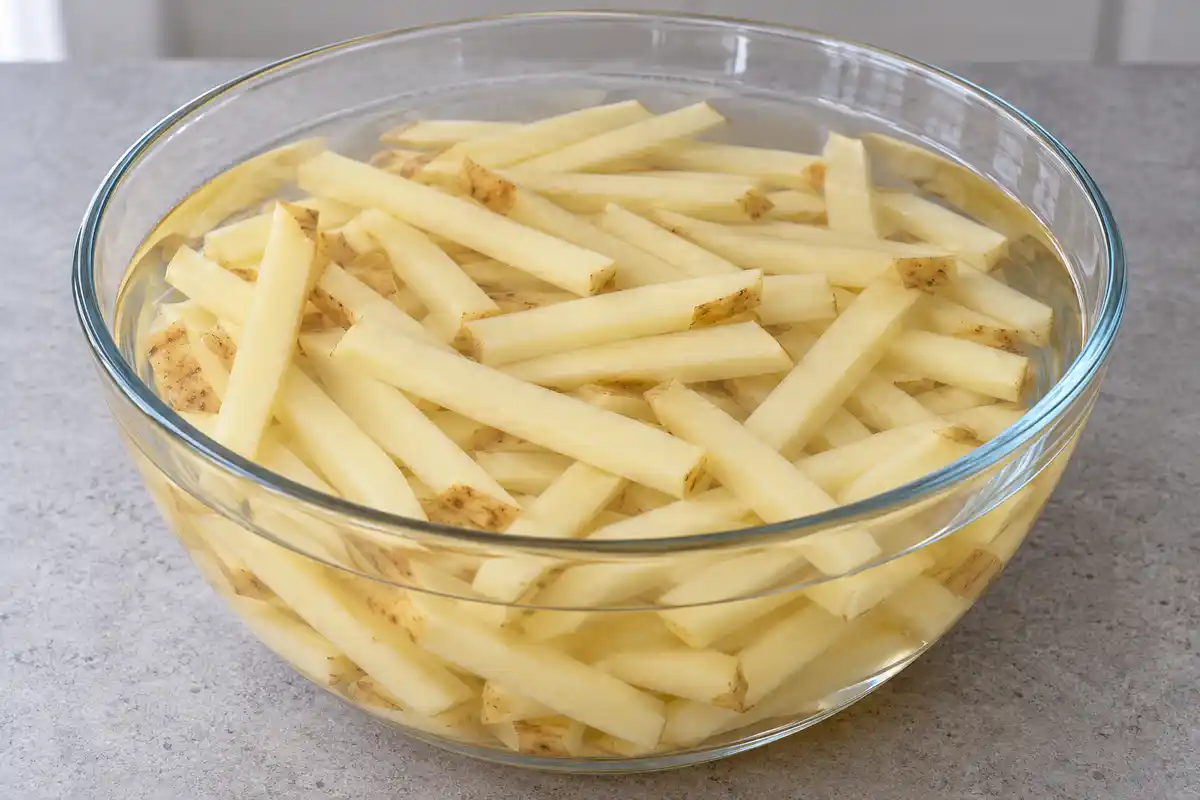 Bâtonnets crus de pomme de terre immergés dans l’eau, à l’étape du trempage avant leur séchage.